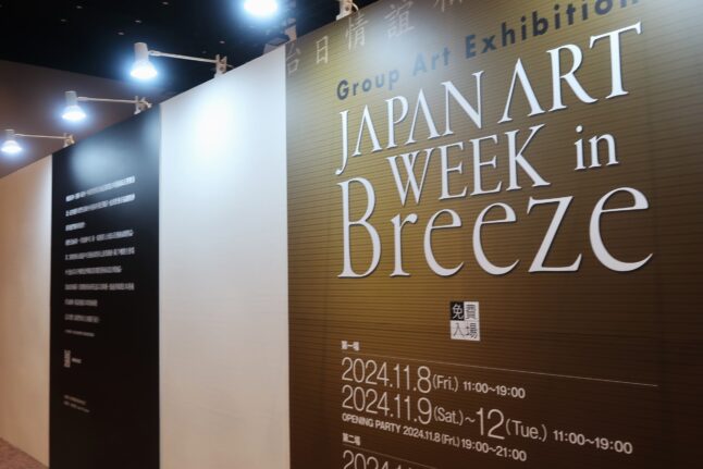 展示会場の入り口のタイトルパネル。ゴールドの地の色に白文字で大きく「JAPAN ART WEEK in Breeze」と書かれている。