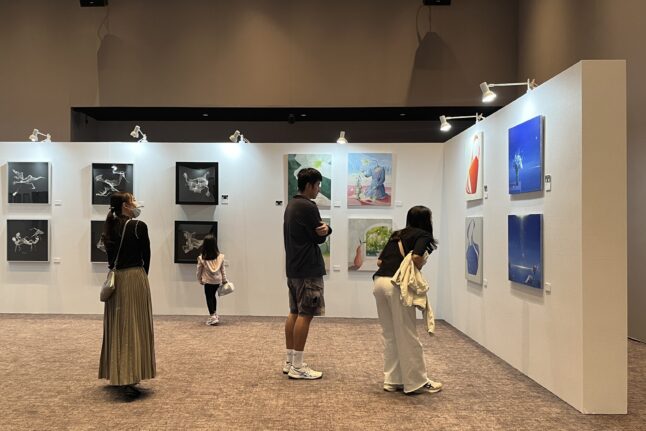 「JAPAN ART WEEK in Breeze」の展示会場。腰を曲げて作品を間近で鑑賞する来場者たち。